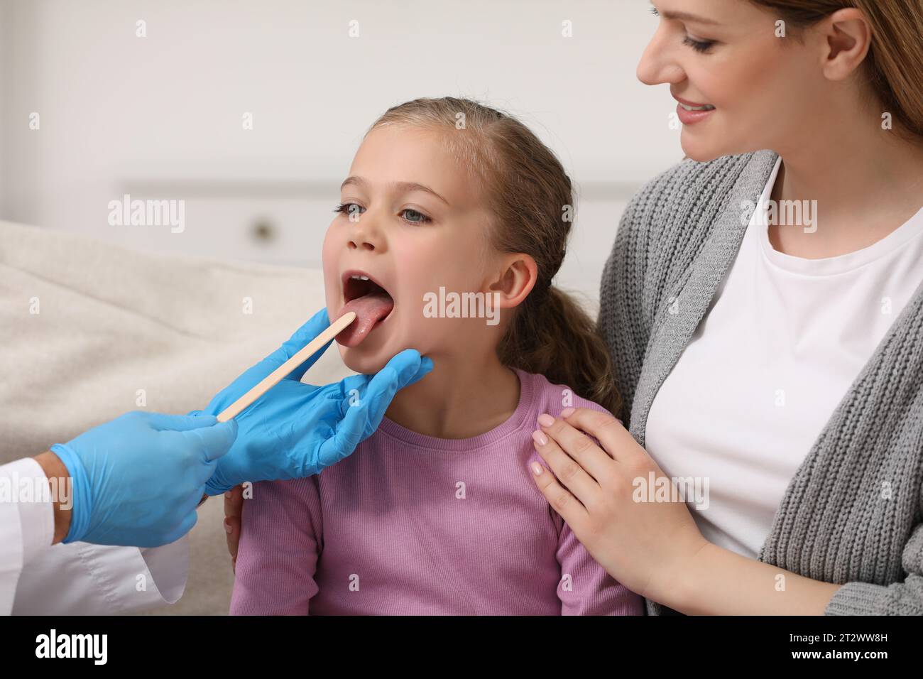 Doctor examining girl`s oral cavity with tongue depressor near her